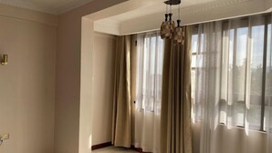 Quarto com uma janela grande, cortinas bege, luminária pendente e piso de azulejos.