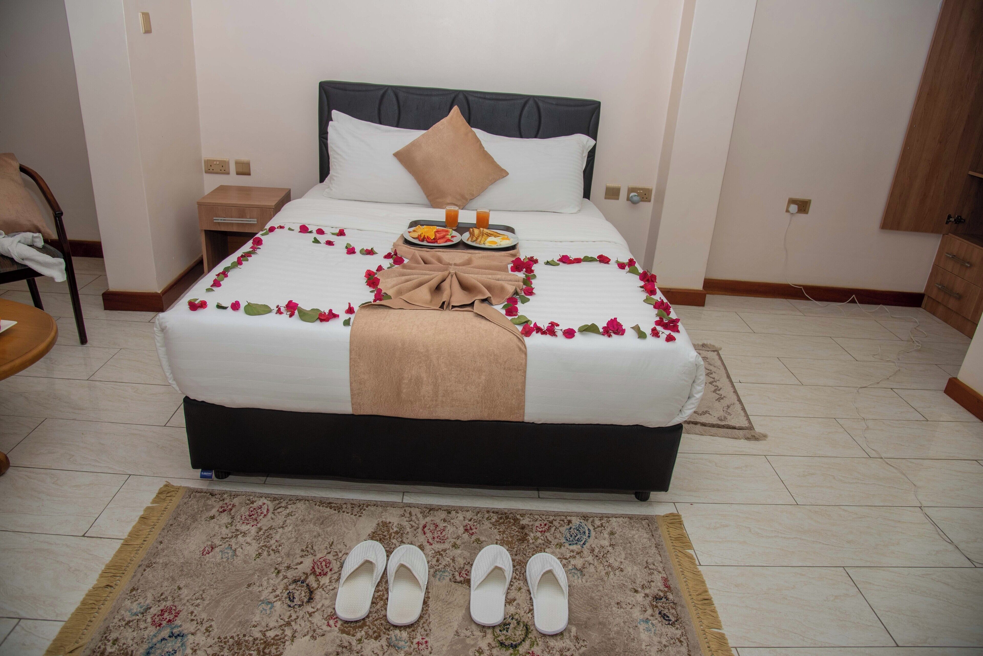 A neatly made bed with a white and brown bedspread, a brown pillow, and a tray of breakfast items on the bed.