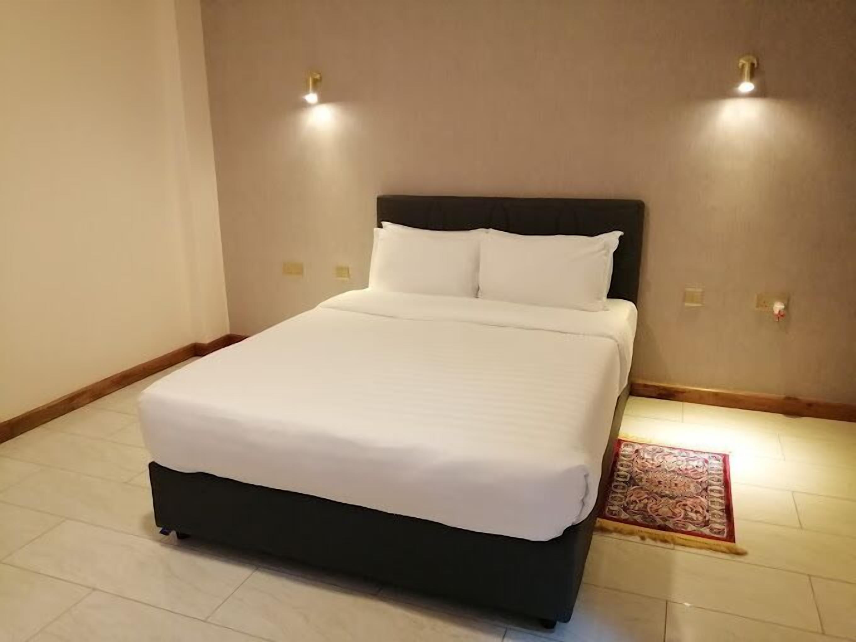 Un lit bien fait, avec du linge de lit blanc, dans une chambre d’hôtel.