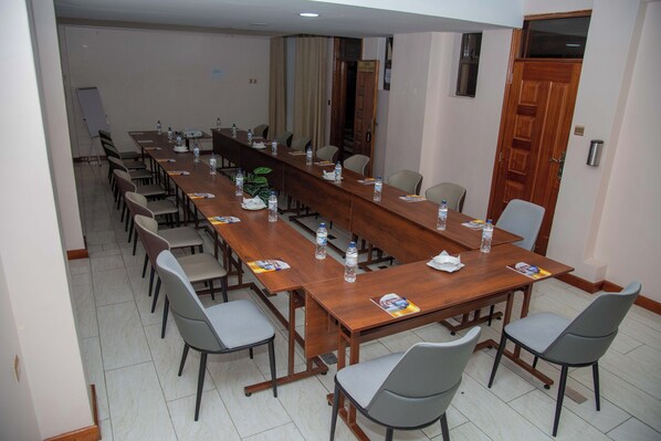 Un salón de conferencias con una larga mesa de madera, varias sillas y botellas de agua.
