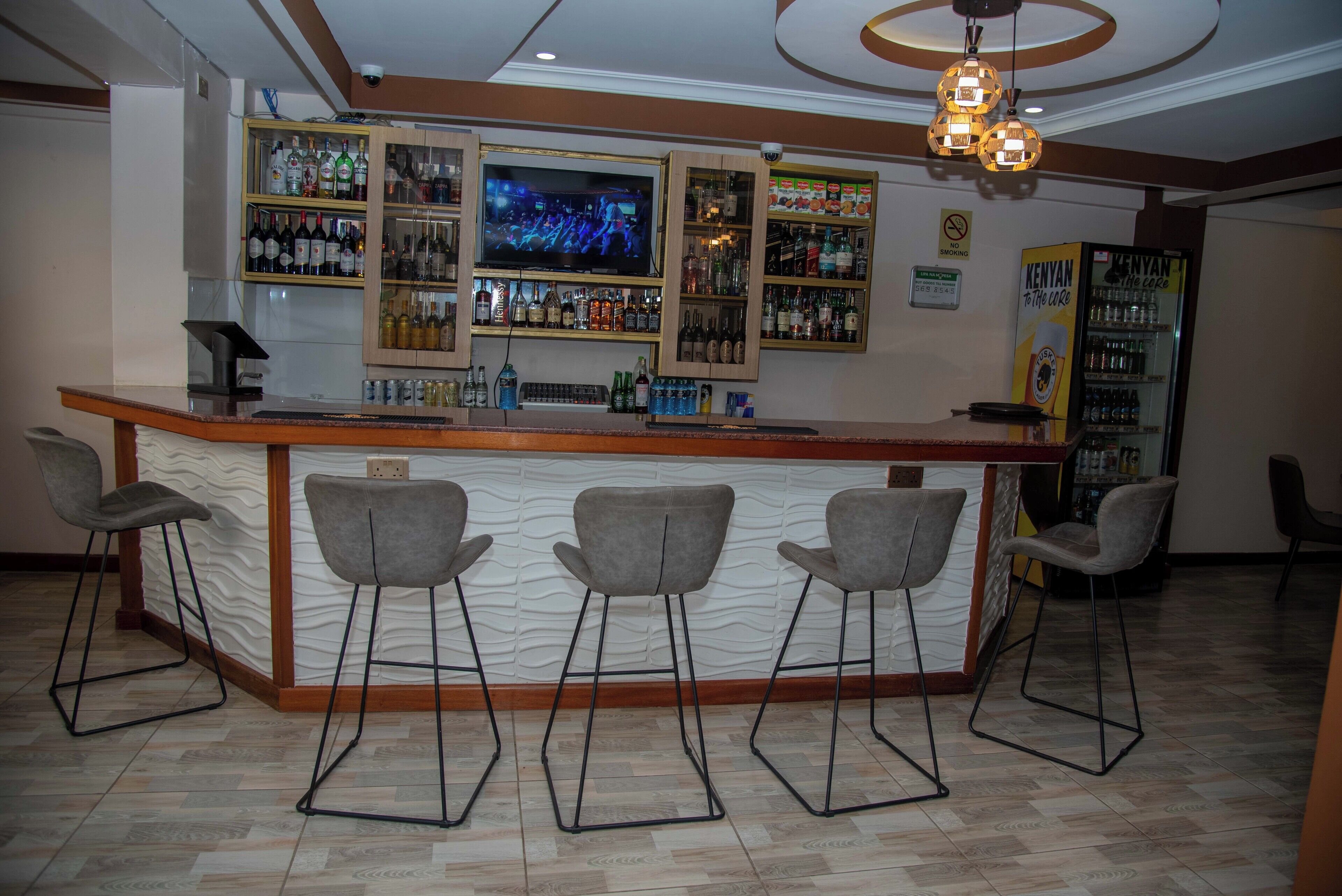 A bar area with a counter, bar stools, a television screen, and shelves with bottles.