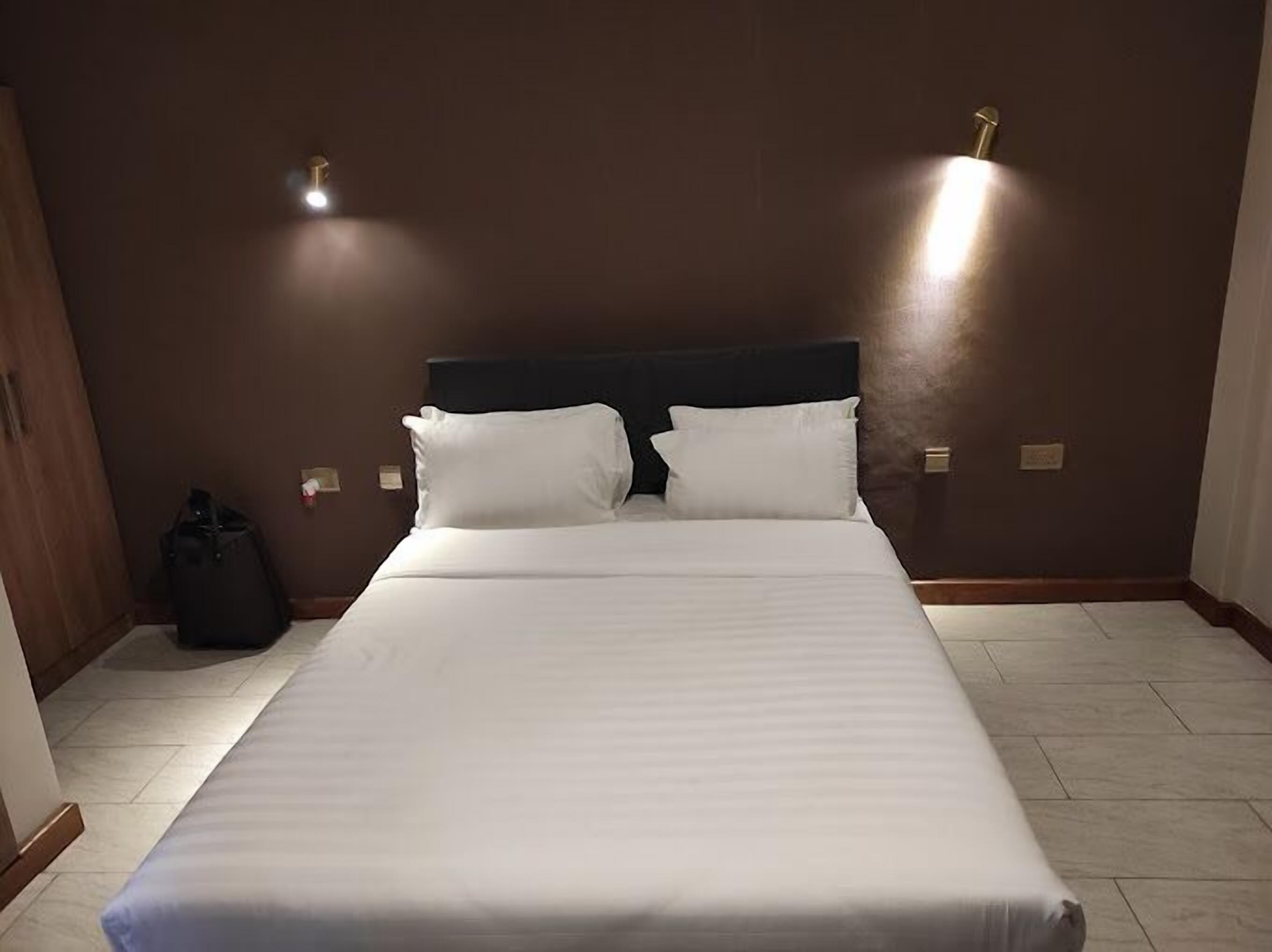 A hotel room with a large bed, two bedside lamps, and a wooden wardrobe.