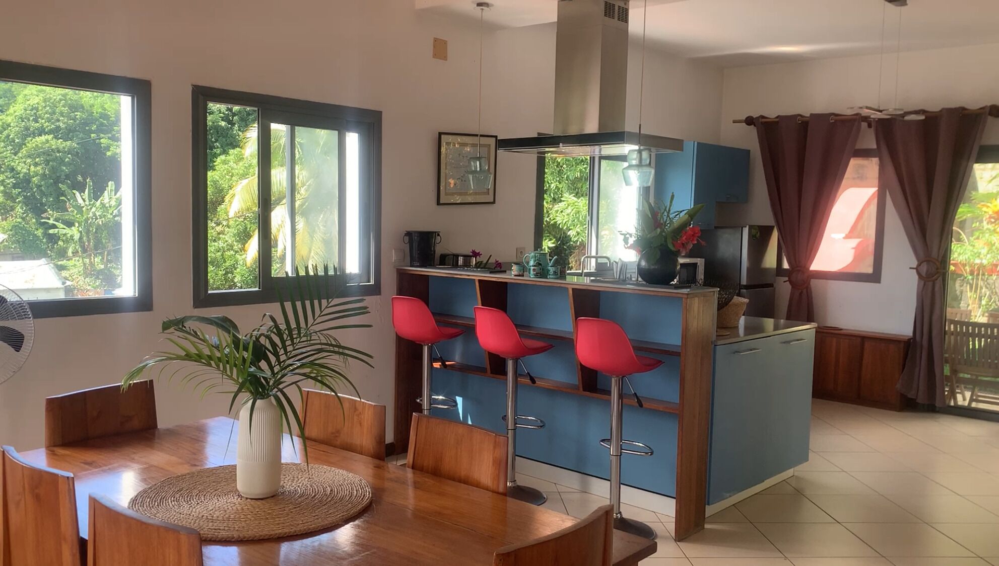 A modern kitchen with a central island, bar stools, and large windows with views of greenery.