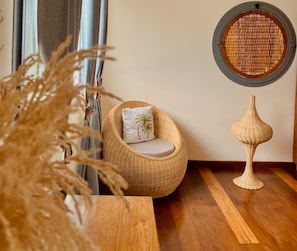 Una silla de mimbre con un cojín y una lámpara decorativa sobre un piso de madera.