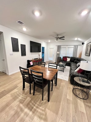 A modern living room with a wooden dining table, black leather sofa, and a ceiling fan.