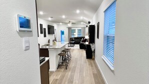 A modern kitchen with a central island, bar stools, and a dining area with a black leather couch. - GIG ’EM LANE • 3BR • Grill & Fire Pit • Coffee Bar • 75" TV • Near Hwy 6 (College Station)