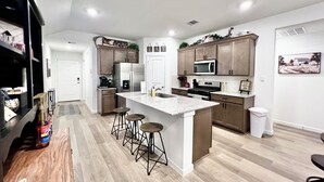 A modern kitchen with a central island, bar stools, stainless steel appliances, and wooden cabinets. - GIG ’EM LANE • 3BR • Grill & Fire Pit • Coffee Bar • 75" TV • Near Hwy 6 (College Station)