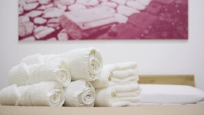 Een stapel witte handdoeken op een houten oppervlak, met een wit kussen en een foto in roze en witte tinten aan de muur.