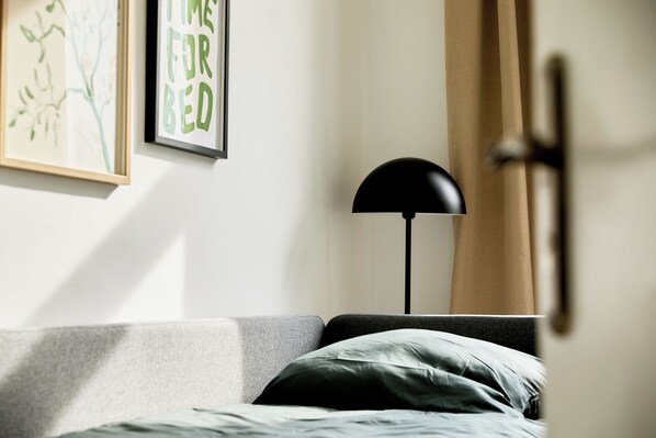A bedroom with a bed, a floor lamp, and two framed artworks on the wall.
