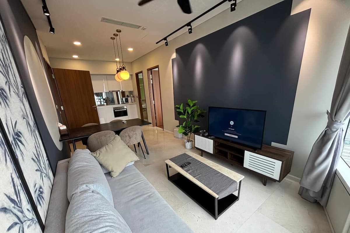 A modern living room with a sofa, coffee table, TV, and a dining area in the background.