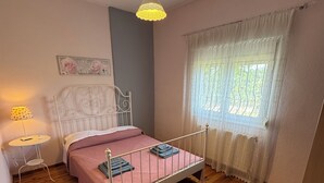 A bedroom with a metal bed frame, a bedside table with a lamp, a window with curtains, and a wall with a decorative sign.