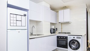A compact kitchen with white cabinets, a built-in oven, a microwave, and a front-loading washing machine.
