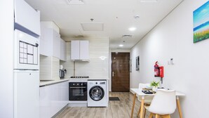 A compact kitchen with a washing machine, a dining area with a table and chairs, and a door leading to another room.
