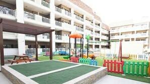 A children's play area with a fenced soccer field, a picnic table, and a playground with colorful equipment.