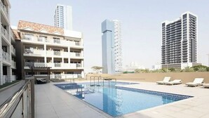 A swimming pool with a tiled deck, surrounded by modern buildings and a clear sky.