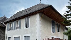Ein zweistöckiges Haus mit rotem Tor, einer kleinen Veranda und einem Abdeckungsdeckel auf der Auffahrt.