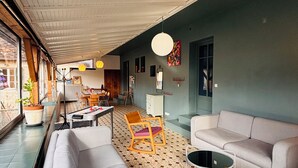 Ein geräumiges Zimmer mit großem Fenster, einer Couch, einem Sessel, einem kleinen Tisch und einer Pendelleuchte.