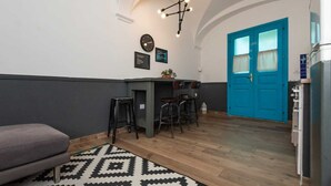 Una cocina compacta con puerta azul, una zona de comedor con taburetes, un reloj y una mesa pequeña con una planta.