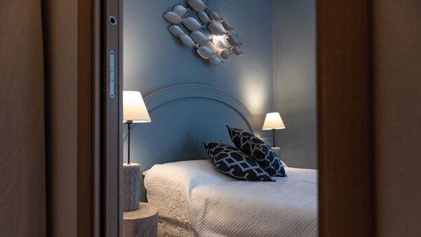 Una cama bien hecha con almohadas estampadas, dos lámparas de noche y una decoración de pared original.