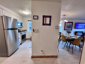 Una cocina moderna con electrodomésticos de acero inoxidable, un comedor con mesa y sillas, y una sala de estar con televisor de pantalla plana.