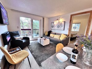 A living room with a sofa, armchair, coffee table, and a television. - Mark IX Alpine Condo • Cozy Mtn Condo • 1 mile to Breck Main St + Slopes (Breckenridge)