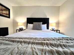 A hotel room with a large bed, two bedside lamps, a headboard, and a wall-mounted clock.