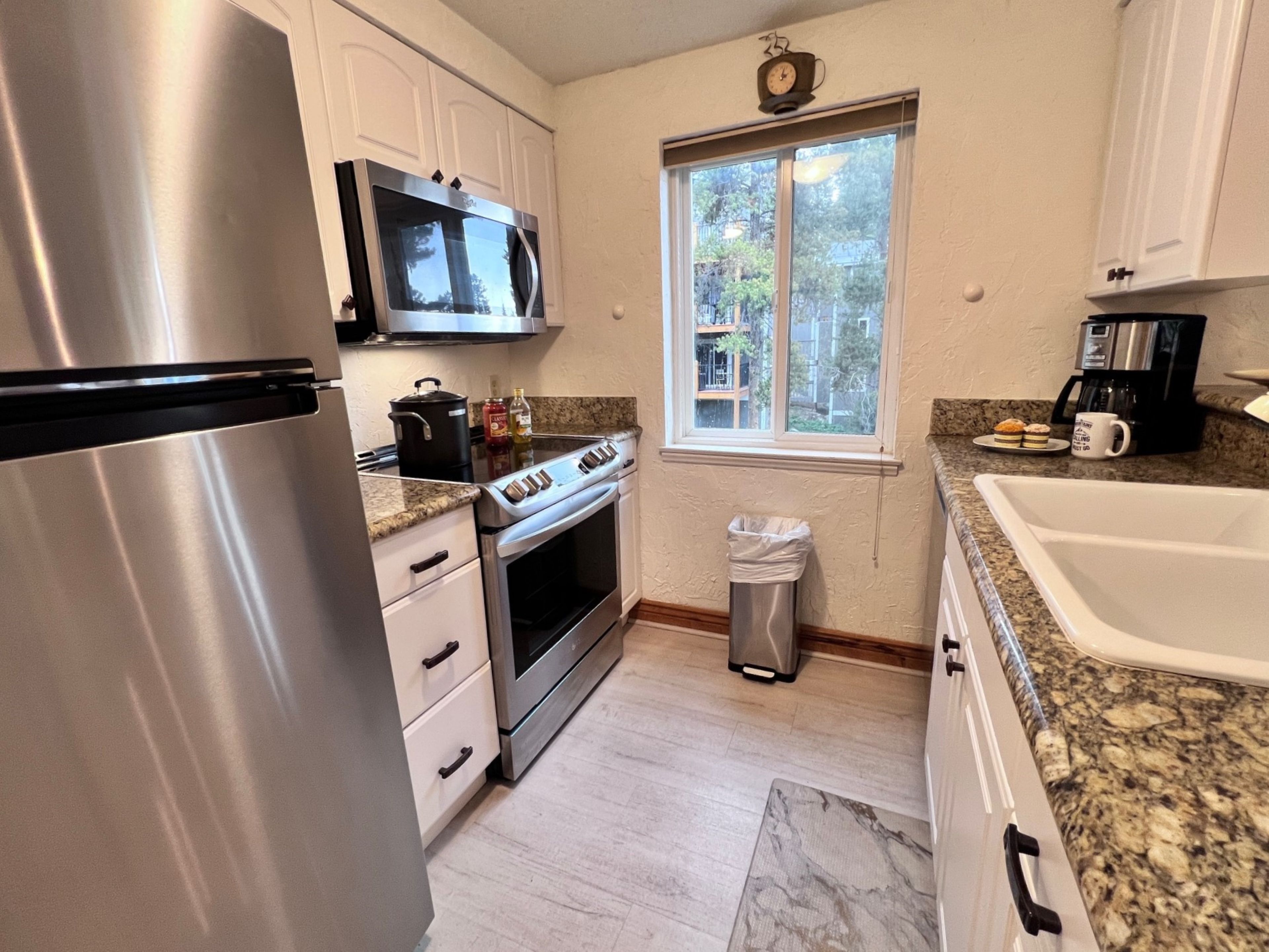 A kitchen with stainless steel appliances, a microwave, a stove, and a window with a view of buildings.