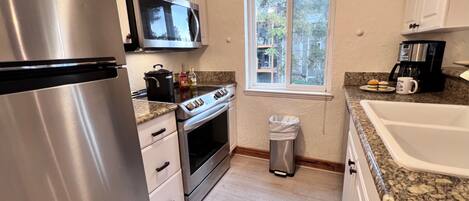 A kitchen with stainless steel appliances, a microwave, a stove, and a window with a view of buildings.