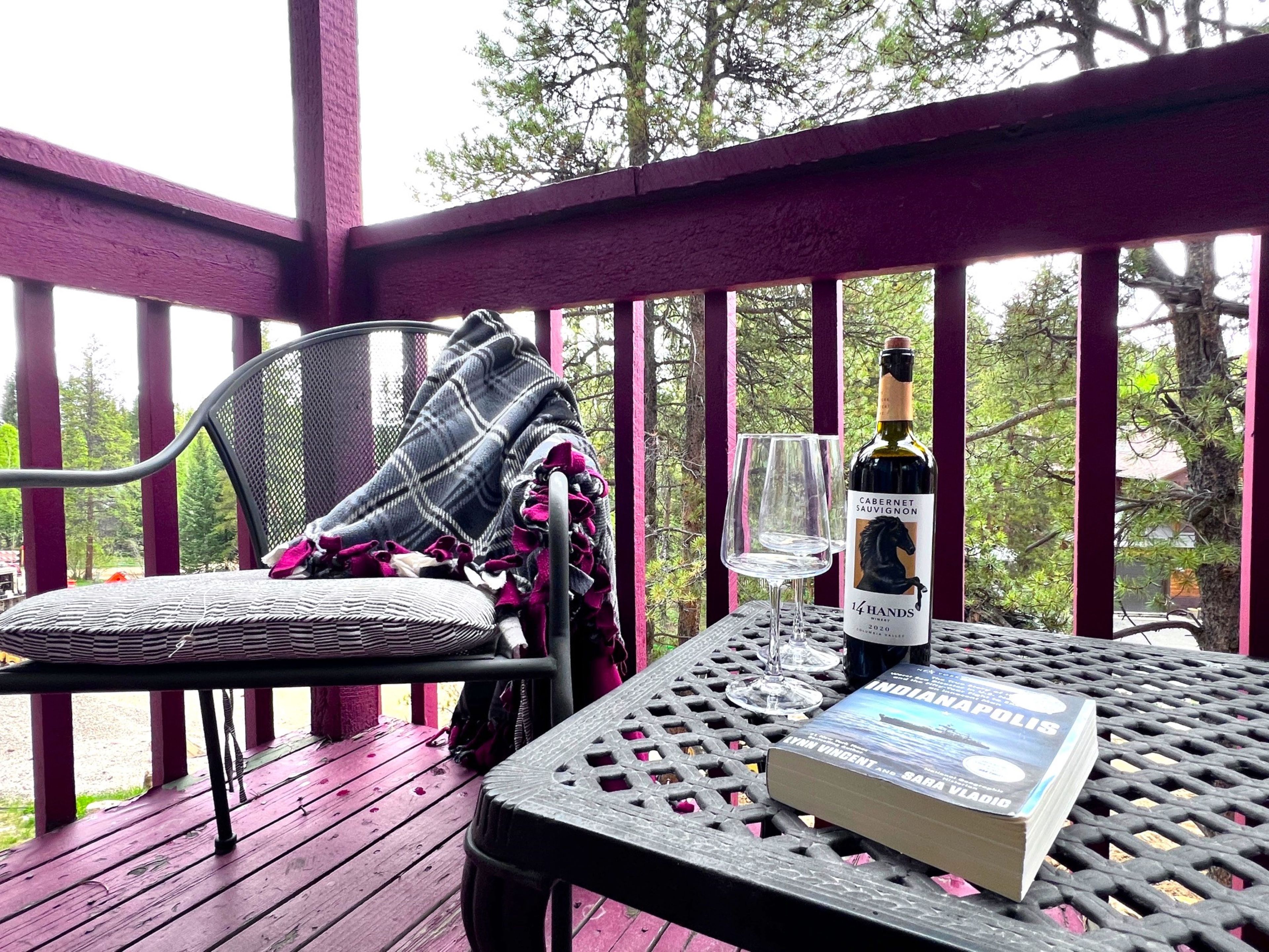 A covered outdoor seating area with a table, a chair, a book, a wine bottle, and a glass.