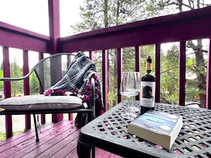 Un espacio al aire libre cubierto con una mesa, una silla, un libro, una botella de vino y una copa.