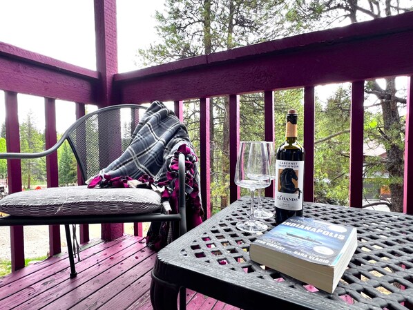 A covered outdoor seating area with a table, a chair, a book, a wine bottle, and a glass.