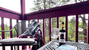 Un espace extérieur abrité, aménagé avec une table, une chaise, une bouteille de vin et un livre.