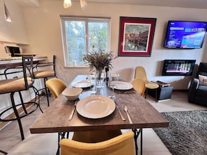 A dining area with a table set for four, a vase with flowers, and a flat-screen TV mounted on the wall.
