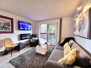 Una sala de estar con televisor de pantalla plana, un sofá, una silla y una mesa de centro.