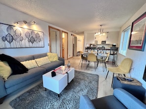 A modern living room with a grey sofa, a white coffee table, and a dining area with chairs and a table.