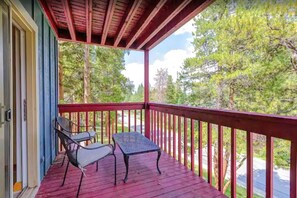 A covered porch with two chairs and a table, overlooking a forested area.