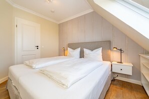 Una cama individual con ropa de cama blanca, una mesita de noche con lámpara y una puerta a la izquierda.