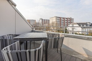 Un balcón con mesa y sillas, con vista a un paisaje urbano de edificios.