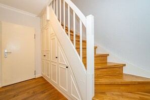 A staircase with wooden steps and white railings, leading to a landing with a door. - Schaumkrönchen - Apartment Schaumkrönchen: Close to the beach with balcony. (Sylt)
