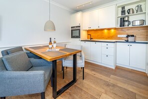A modern kitchen with white cabinets, a wooden countertop, and a built-in oven. There is a dining area with a wooden table and grey upholstered chairs. - Schaumkrönchen - Apartment Schaumkrönchen: Close to the beach with balcony. (Sylt)
