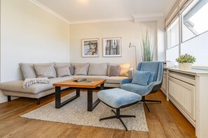 A modern living room with a sectional sofa, a blue armchair, a coffee table, and two framed artworks on the wall. - Schaumkrönchen - Apartment Schaumkrönchen: Close to the beach with balcony. (Sylt)