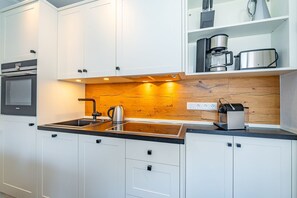 A modern kitchen with white cabinets, a wooden backsplash, and stainless steel appliances. - Schaumkrönchen - Apartment Schaumkrönchen: Close to the beach with balcony. (Sylt)