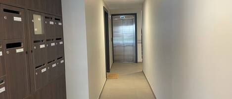 A hallway with lockers on the left, a door at the end, and a ceiling with a grid pattern.