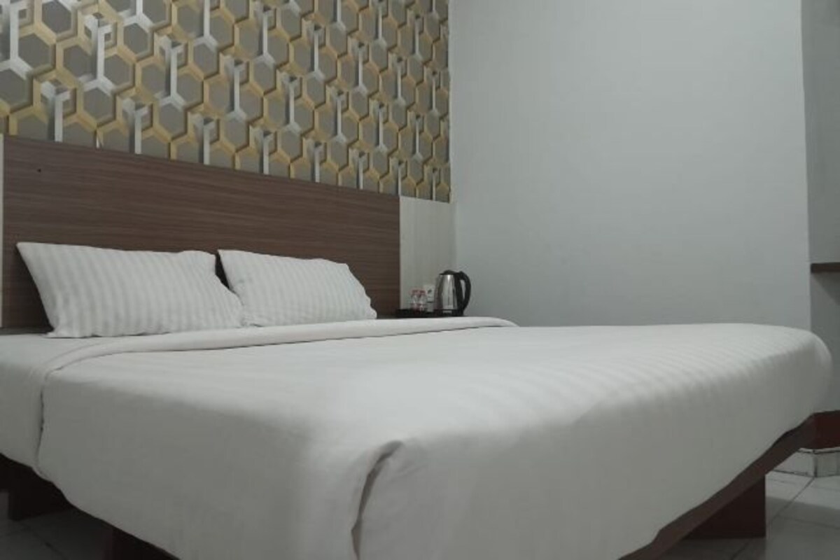 A neatly made bed with white linens, a wooden headboard, and a patterned wall behind it.