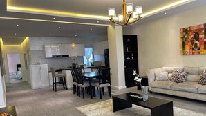 A modern living room with a black coffee table, a sofa with patterned cushions, and a dining area with a dark wooden table and chairs. - Luxurious 3-bedroom apartment with WiFi in Bole Addis (Addis)
