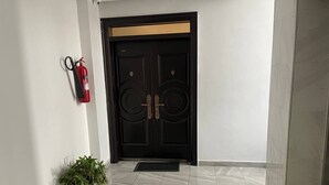 A black double door with a gold accent, a fire extinguisher on the wall, and a potted plant in the entrance area. - Luxurious 3-bedroom apartment with WiFi in Bole Addis (Addis)