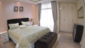 A bedroom with a large bed, a nightstand, a bench, a wardrobe, and a television. - Luxurious 3-bedroom apartment with WiFi in Bole Addis (Addis)