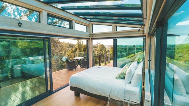 Camera moderna con un letto grande, un tavolino e vista su una terrazza e vegetazione.