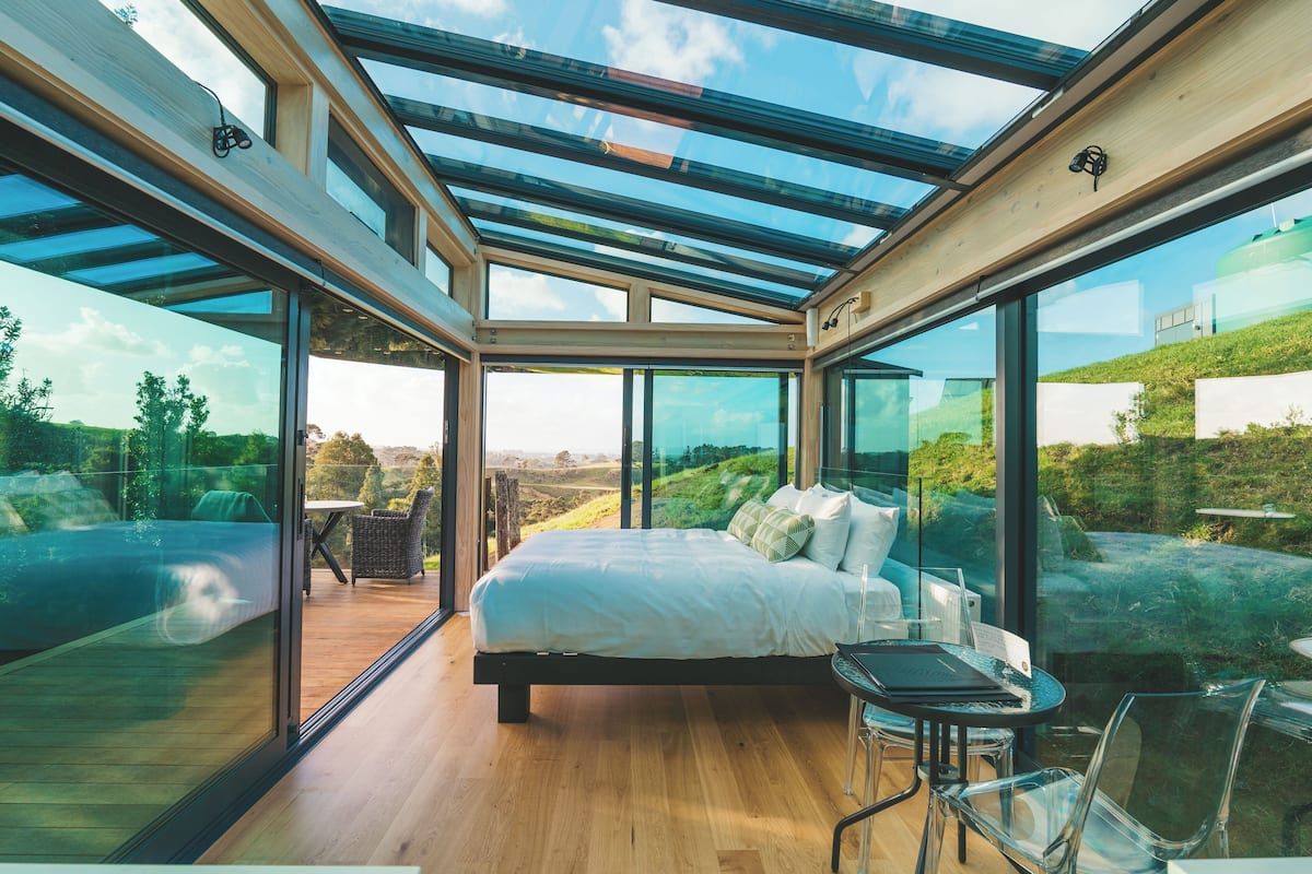 Un dormitorio moderno con techo de cristal, una cama grande y un área de comedor con mesa y sillas.
