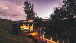 Una casa moderna con facciata in vetro, terrazza in legno e vialetto che conduce all'ingresso.